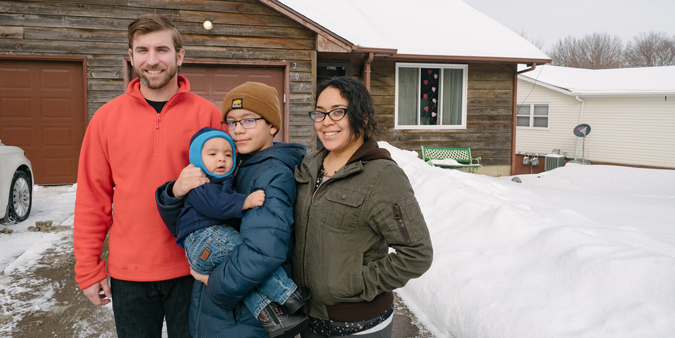 Members stand in front of their first home with their children